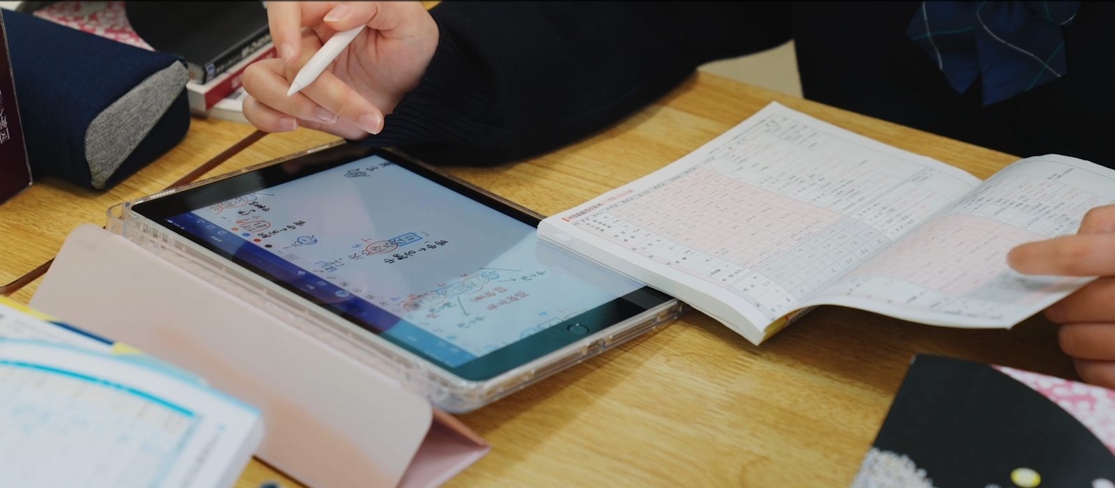 iPadにスタイラスペンで書きこみながら、問題集を開いて学ぶ生徒の手元